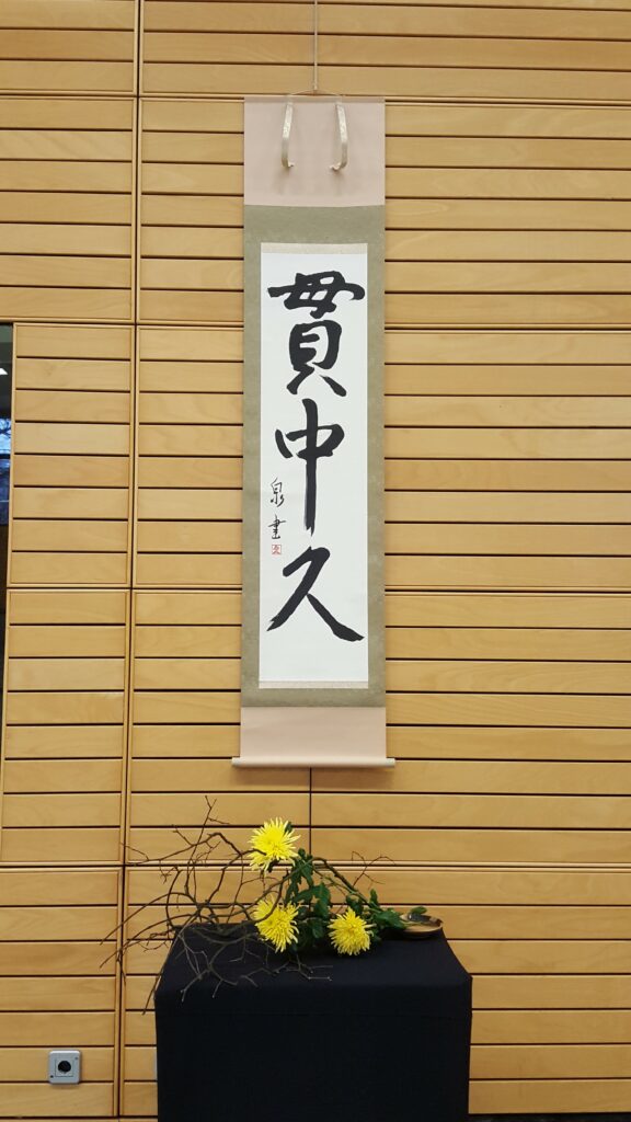 Kamiza zu einem Lehrgang mit unserem Rollbild "Kan Chu Kyu" und einem Blumengesteck aus Zweigen mit Crysanthemen darunter.